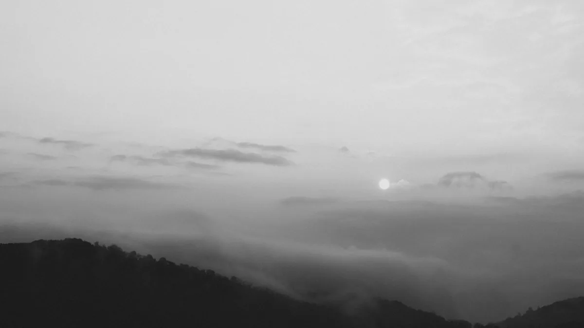 Serene black and white landscape of foggy mountains at dawn with a rising sun.